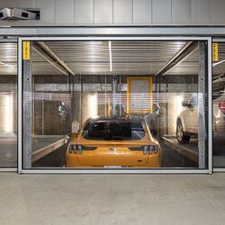 Das Bild zeigt einen gelben Sportwagen in einem Parksystem innerhalb einer modernen Tiefgarage.