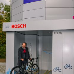 Mann steht mit Fahrrad vor dem Eingang eines automatischen Fahrradparkturms
