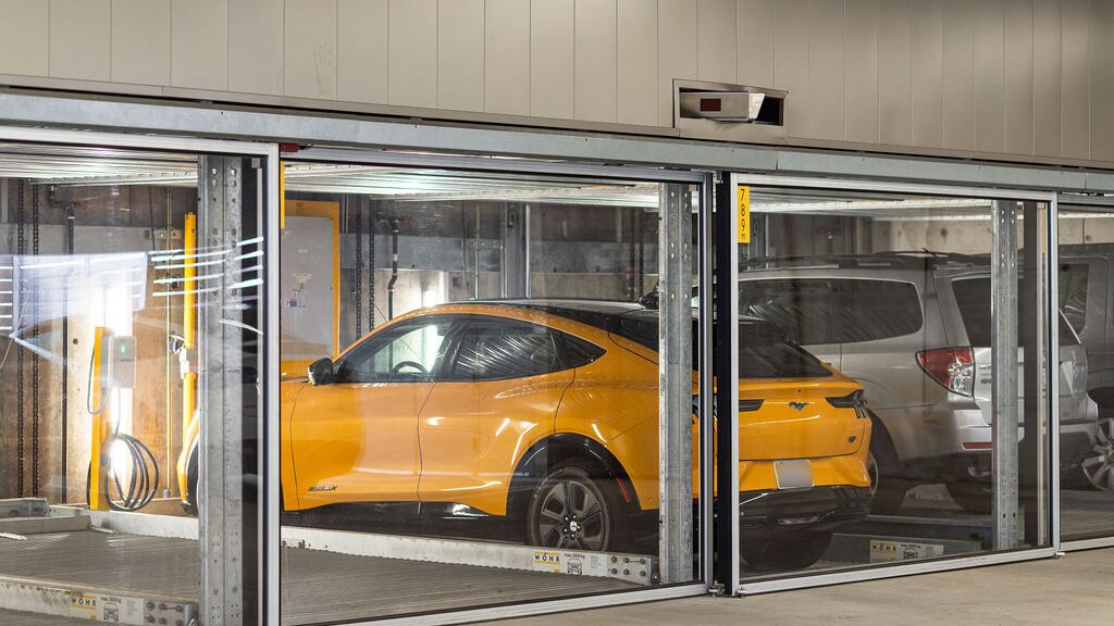 Das Bild zeigt mehrere Fahrzeuge in verglasten Stellplätzen eines Parksystems in einer modernen Tiefgarage.