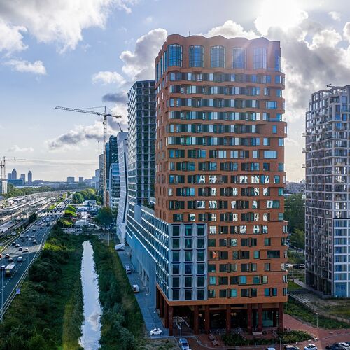 Außenansicht des Projekts The Pulse in Amsterdam mit modernen Hochhäusern und urbaner Verkehrsinfrastruktur.