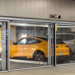 Das Bild zeigt mehrere Fahrzeuge in verglasten Stellplätzen eines Parksystems in einer modernen Tiefgarage.
