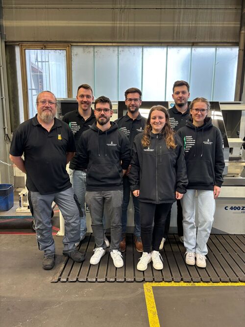 Sieben Personen auf einem Gruppenfoto in der Produktionshalle
