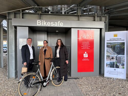 Drei Personen stehen mit einem Fahrrad vor dem Eingang des automatischen Fahrradparksystems